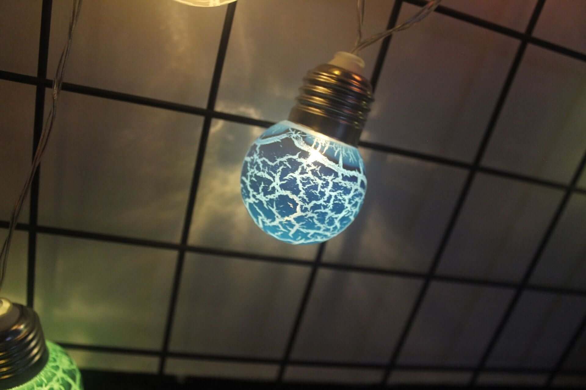 Ampoule LED fissurée bleue éclairant une chaîne de décorations, idéale pour événements et fêtes.