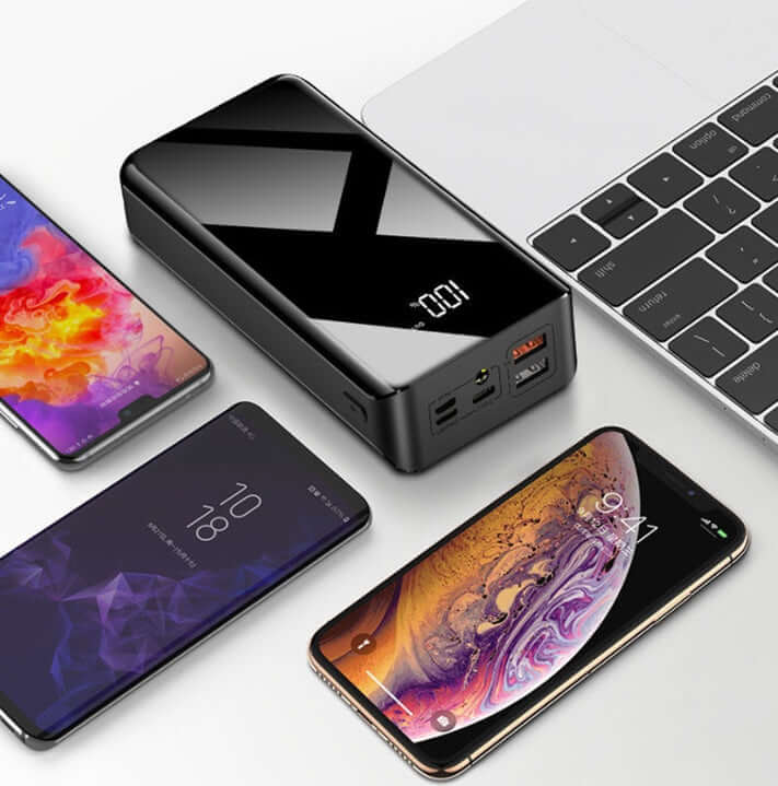 30000mAh power bank with LCD display and multiple device compatibility, placed next to smartphones and a laptop.