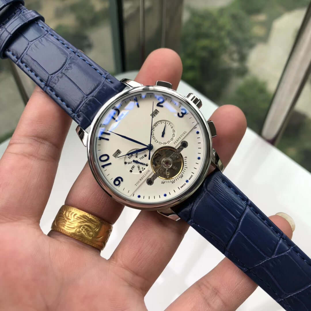 Close-up of a big flywheel mechanical watch with blue strap, showcasing small three needle and calendar functions.