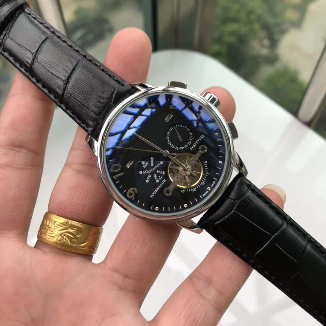Big flywheel mechanical watch with black leather strap, round dial, and calendar display in hand.