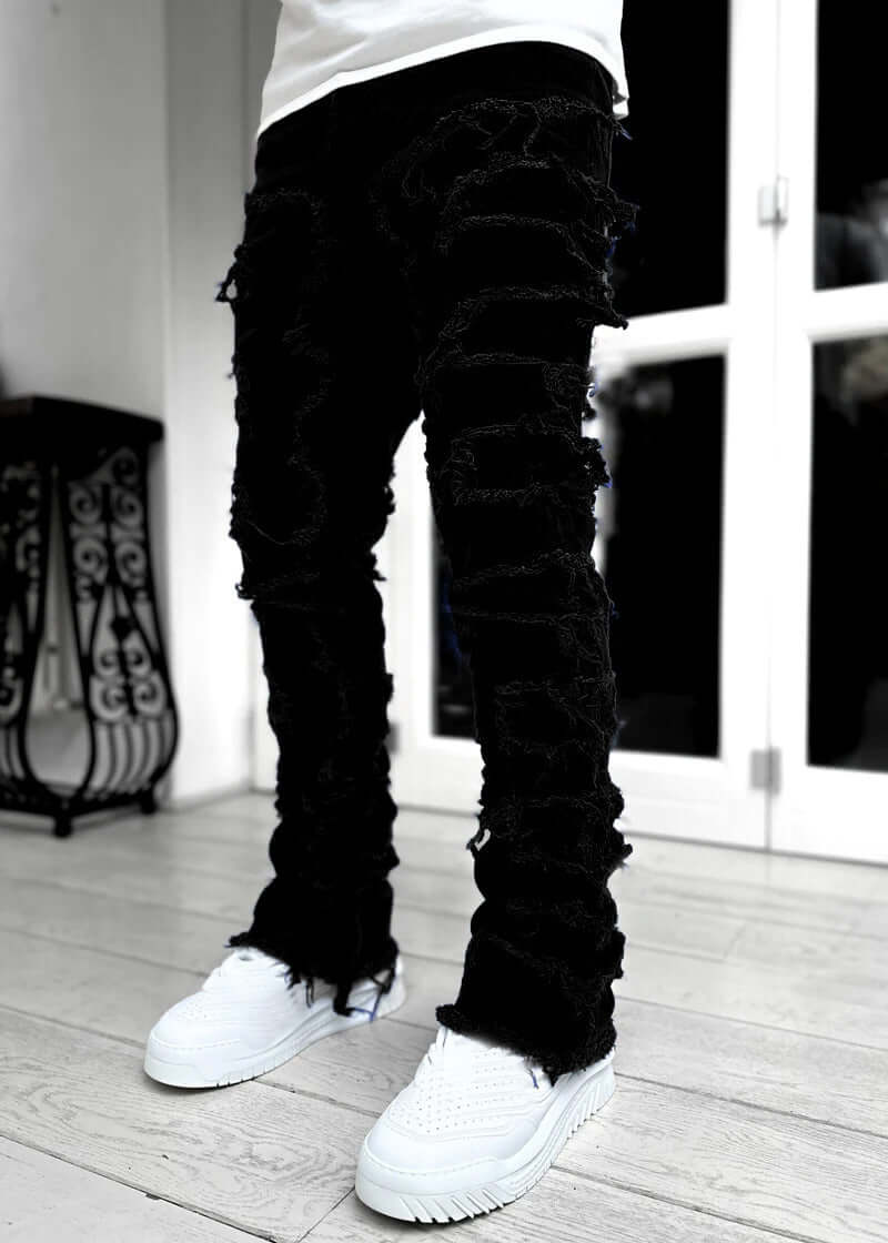 Men's black patched trousers with distressed details, styled with white sneakers for a trendy look.