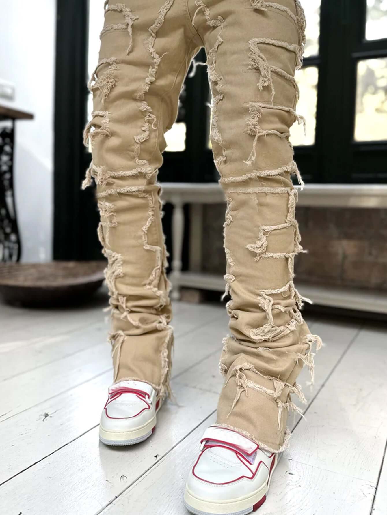 Men's stylish patched pants in beige with frayed details, paired with trendy white sneakers.