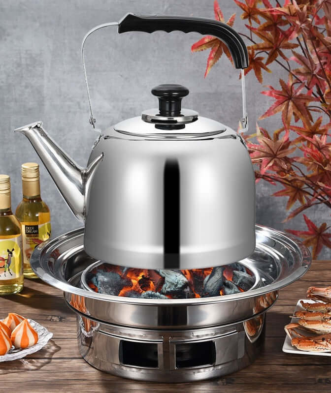 Elegant stainless steel kettle on charcoal grill with flames, surrounded by dishes and bottles, showcasing Korean barbecue style.