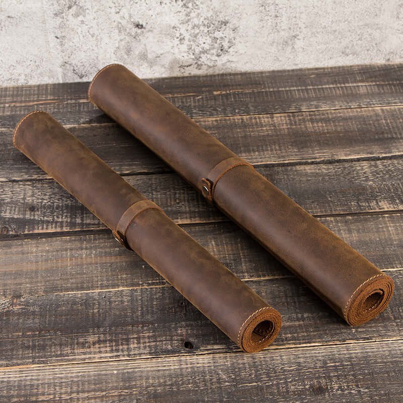 Two rolled extra large non-slip leather desk pads on a wooden surface, showcasing retro style and antiskid features.