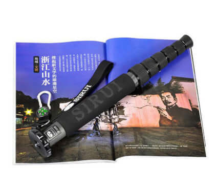 Carbon fiber monopod for SLR camera resting on an open magazine, featuring compass and adjustable sections.