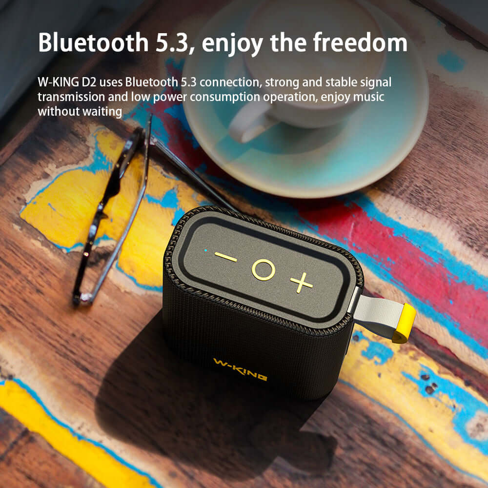 Black Bluetooth speaker with Bluetooth 5.3, featuring volume controls and compact design on wooden surface.