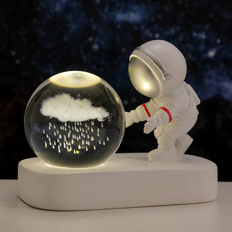 Astronaut figurine beside a glowing crystal ball night light with rain design, perfect for creating a cozy atmosphere.