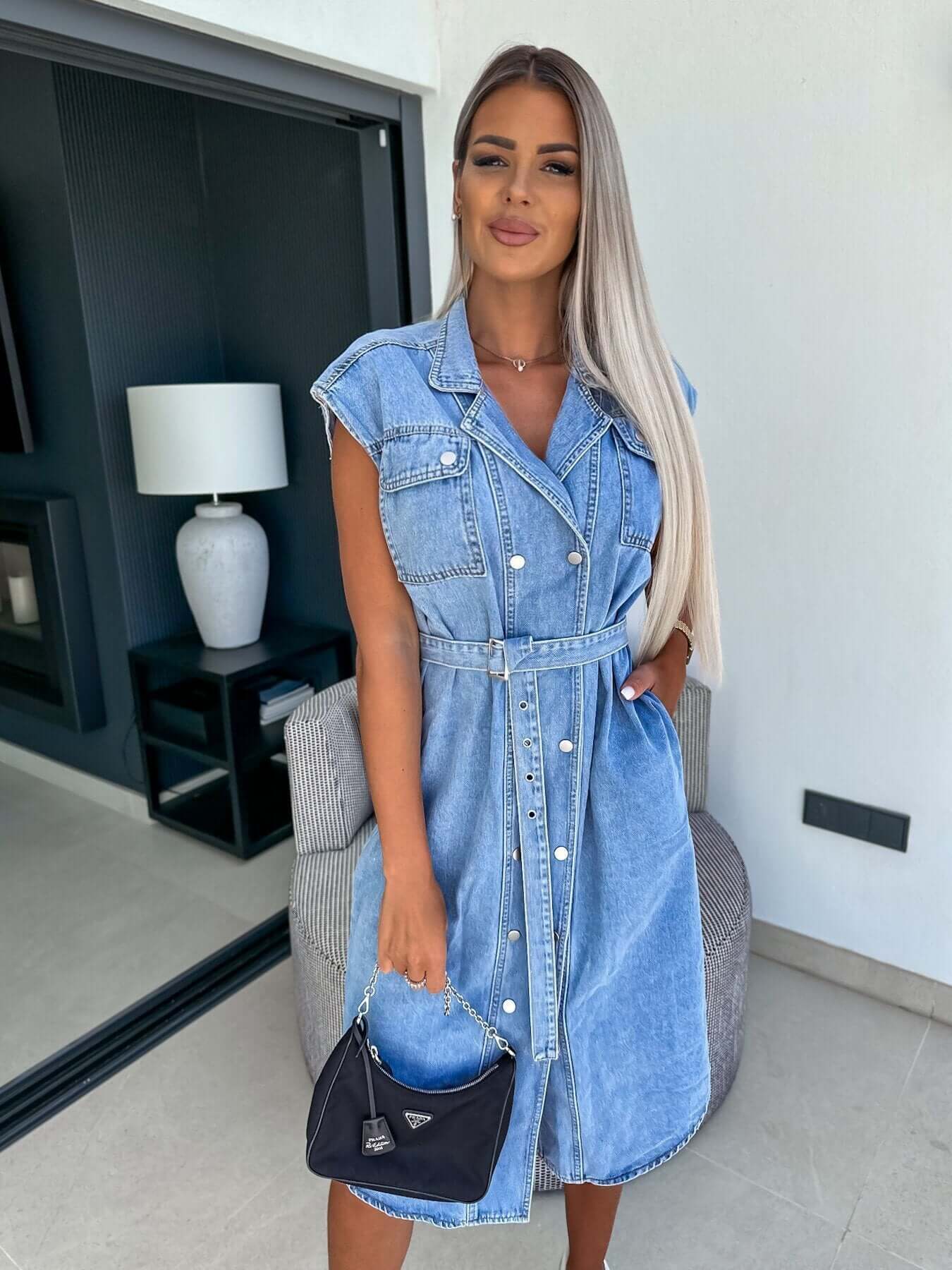 Model wearing a casual sleeveless denim dress with a waist-controlled lace-up design and pockets.