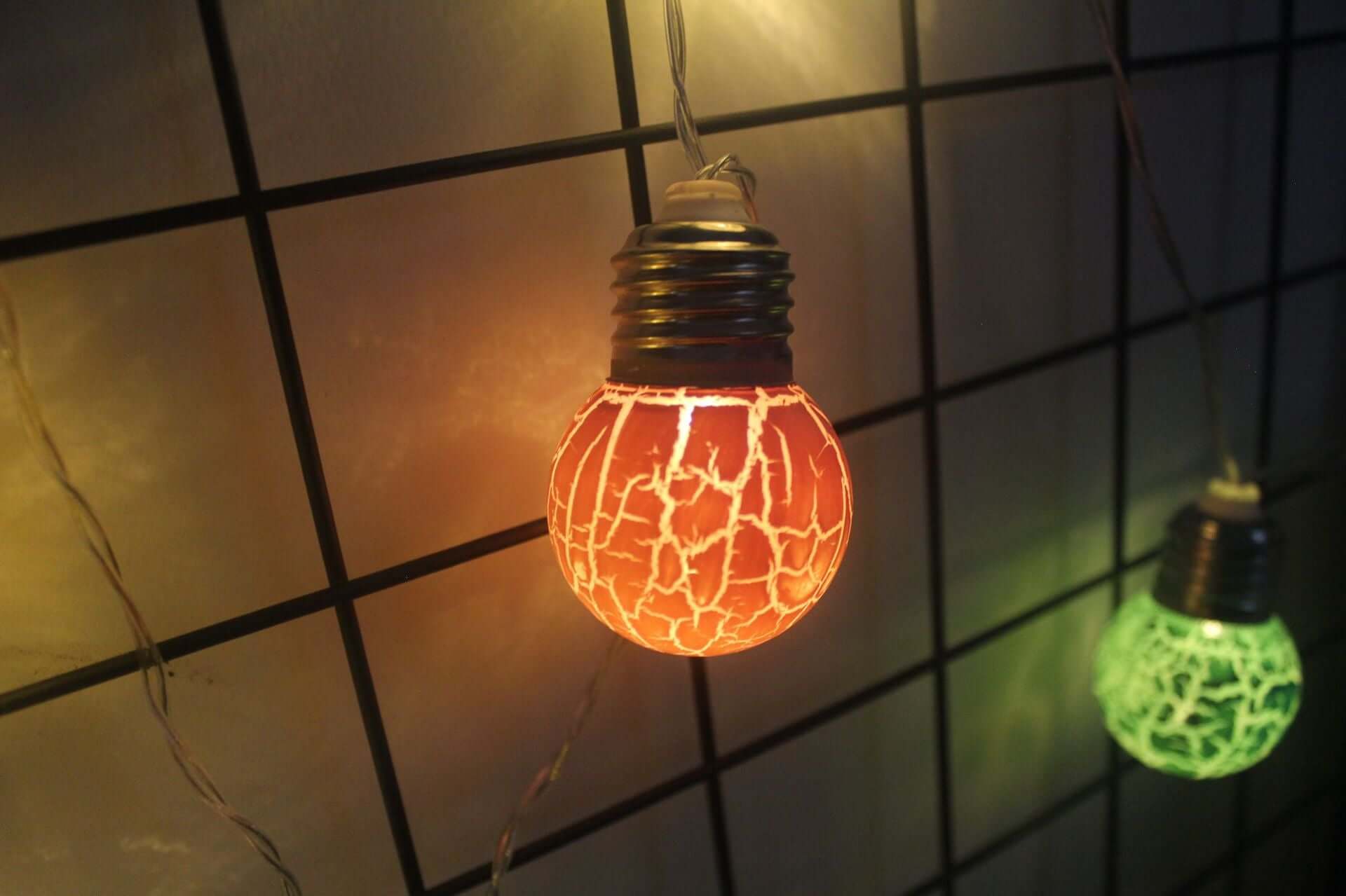 Ampoules LED fissurées orange et verte sur une chaîne décorative, parfaites pour fêtes et déco intérieure.