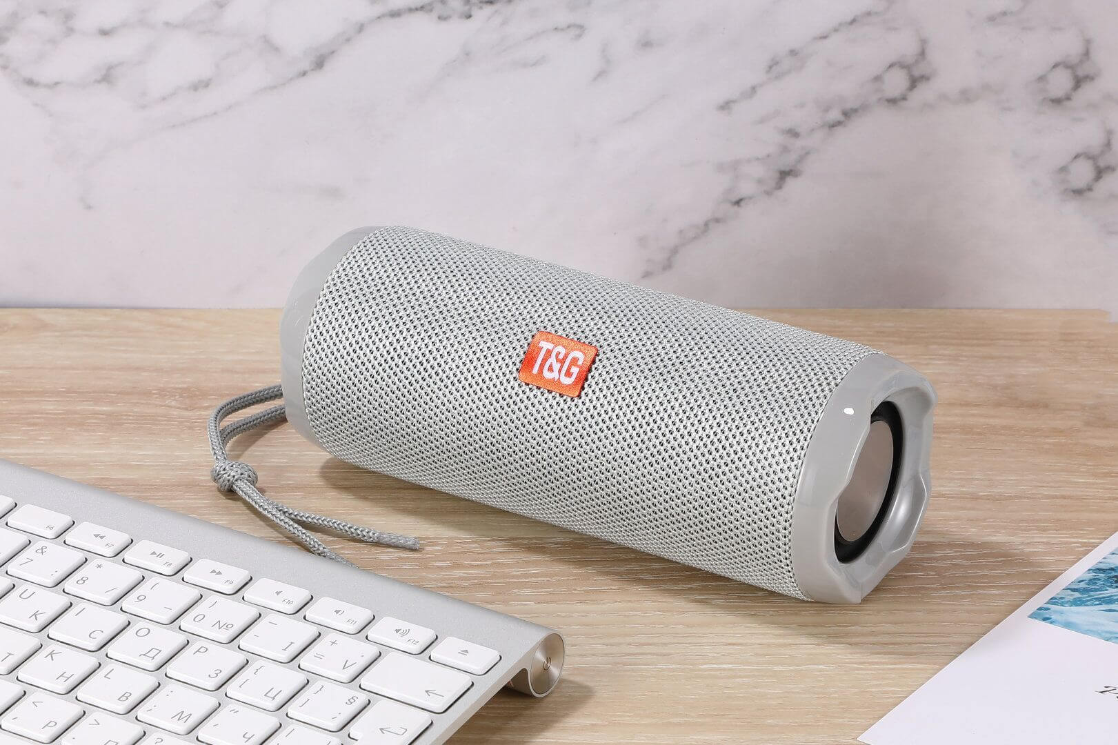 Fabric Portable Creative Wireless Bluetooth Speaker in grey, placed next to a keyboard on a wooden surface.