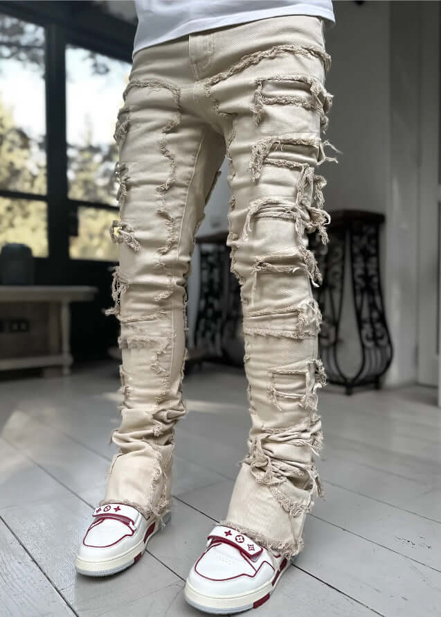 Men's ripped and patched beige jeans with a trendy stacked fit and street style, paired with stylish sneakers.