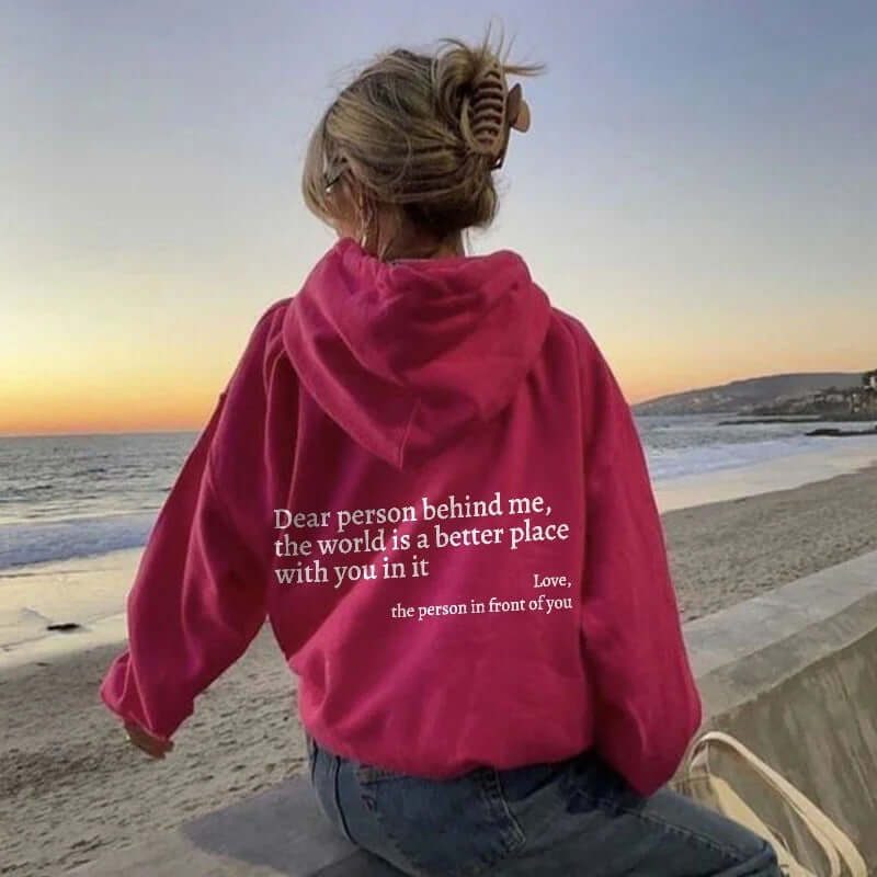 Pink hoodie with inspirational quote on back, worn by person at beach during sunset.
