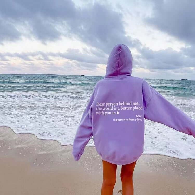 Lavender unisex hoodie on beach with text 'Dear person behind me, the world is a better place with you in it'.