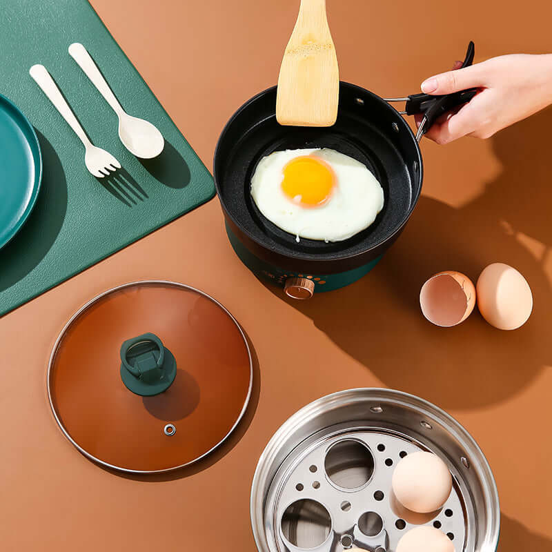 Person frying an egg in a pan with a glass lid, surrounded by plates, utensils, and eggs on a colorful countertop.
