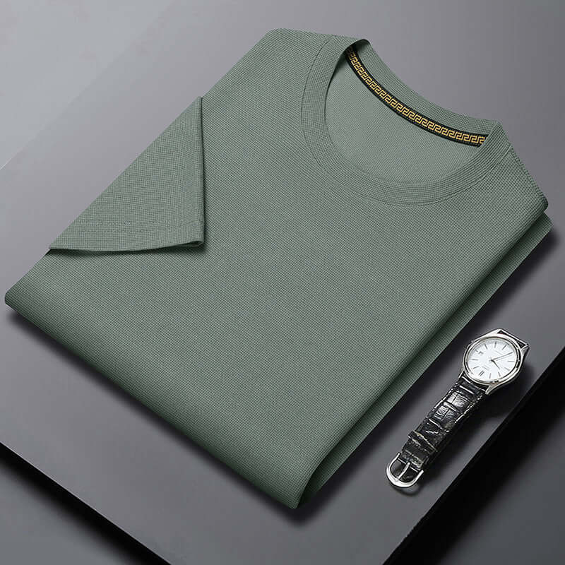 Men's half sleeve round neck top in muted green fabric, displayed with a stylish watch on a sleek background.